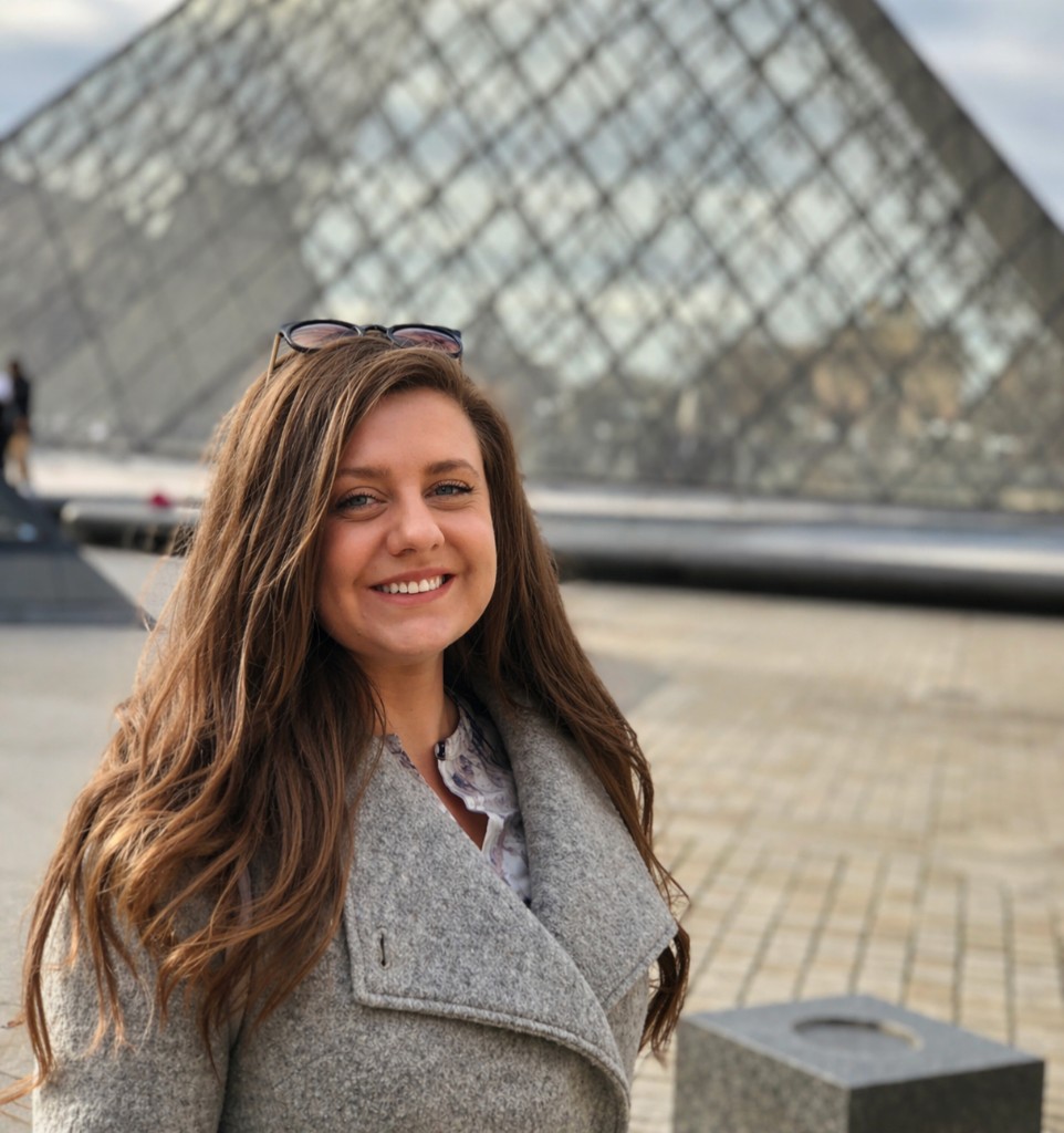 Portrait of Militsa Yanakieva smiling in front of the Louvre Pyramid in Paris