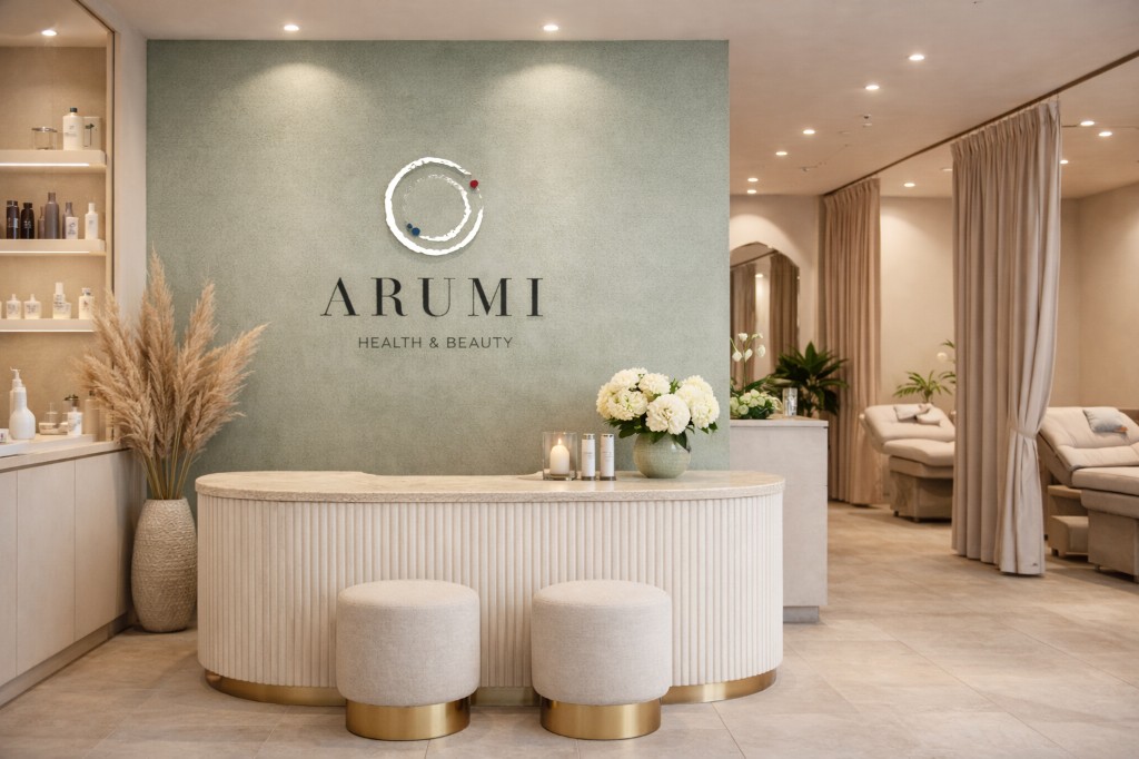 Arumi salon interior — sage feature wall with logo, curved reception desk, hydrangeas and treatment area beyond